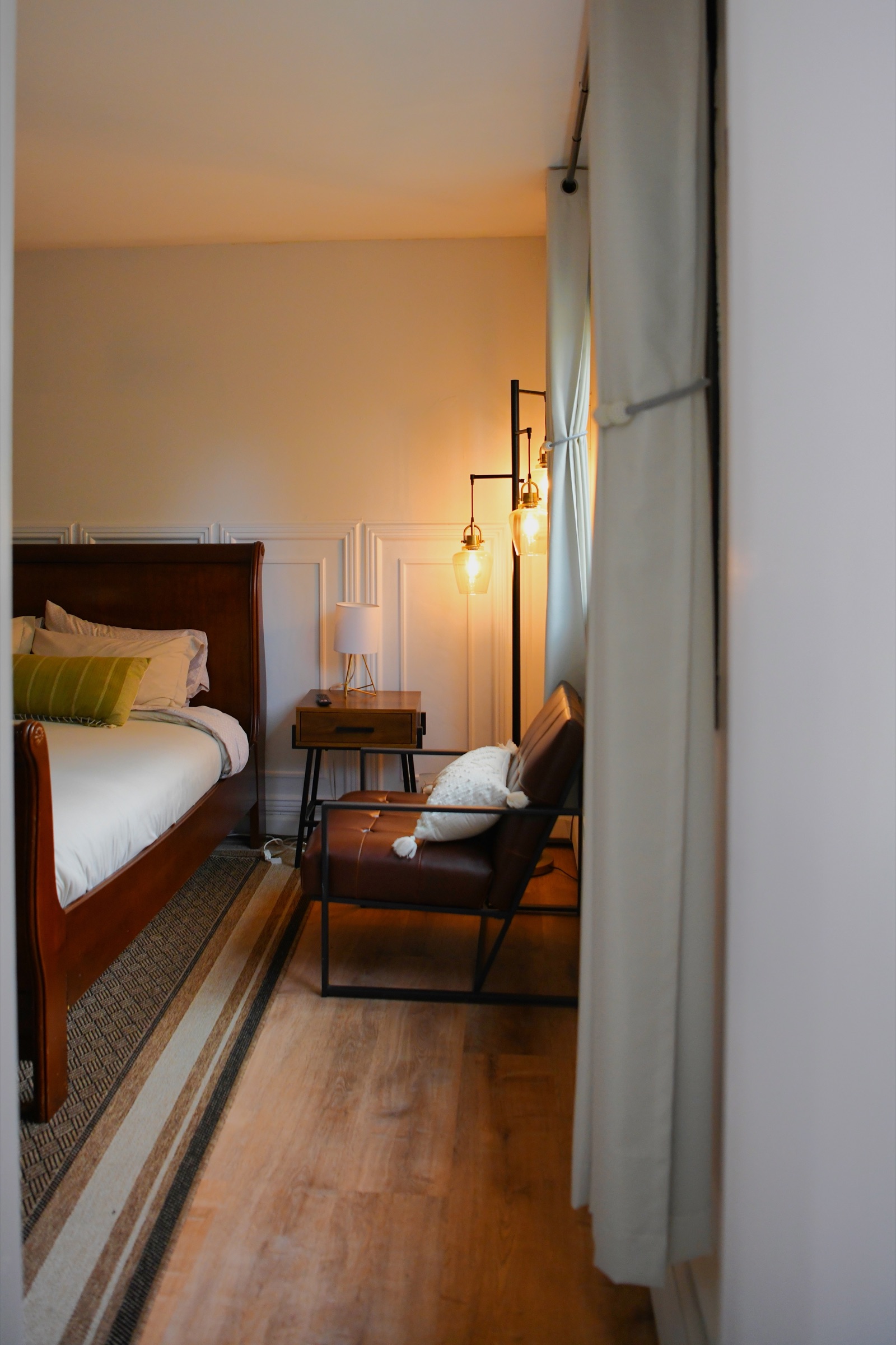 Warm lamplight on a sleigh bed, nightstand and leather armchair seen through a doorway